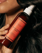 Hand holding Ceremonia Guava Rescue Spray bottle against glossy dark hair, a UV and heat protective detangler.