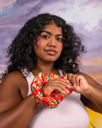 Person with curly hair holding the red guava-print Ceremonia satin scrunchie at chest level.
