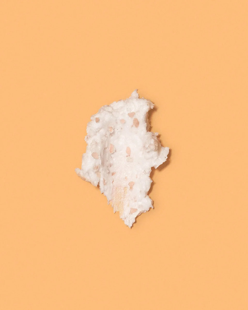 Swatch of whipped white papaya scalp scrub with pink salt exfoliating granules on an orange background.