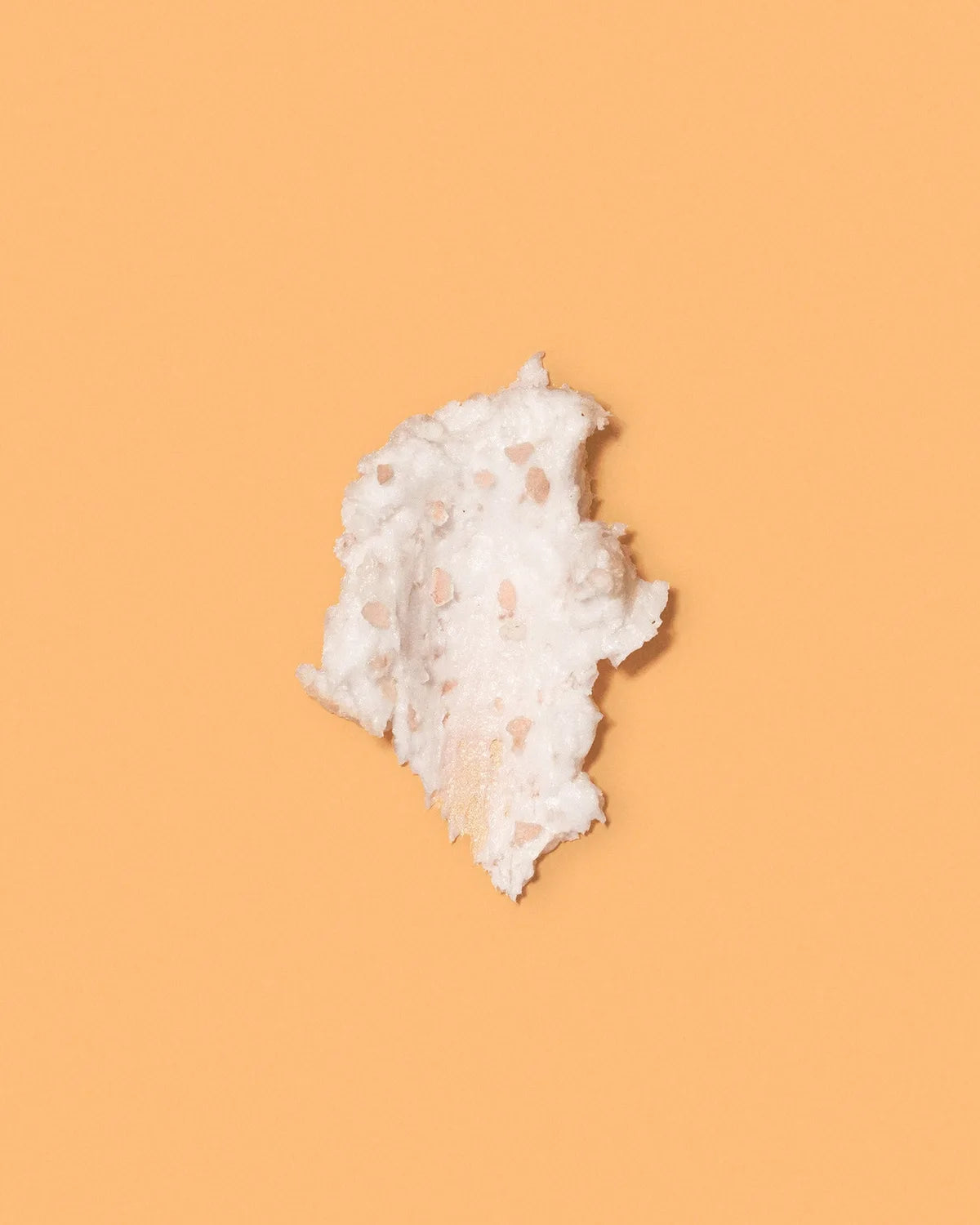 Swatch of whipped white papaya scalp scrub with pink salt exfoliating granules on an orange background.