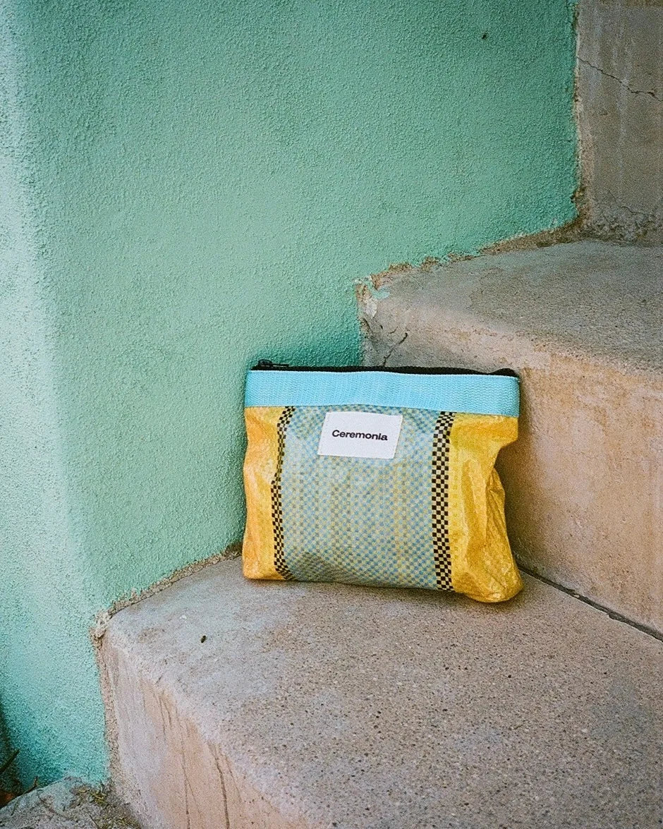 Upcycled woven Ceremonia Pouch de Mercado resting on concrete steps beside a mint green wall.