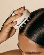 White Ceremonia scalp massager pressed against dark hair to exfoliate and stimulate the scalp.