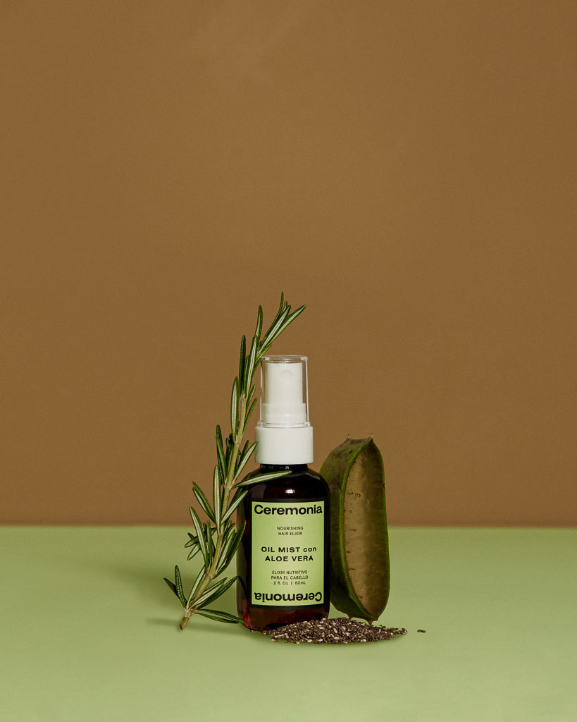 Ceremonia Oil Mist con Aloe Vera bottle beside fresh rosemary, aloe leaf, and chia seeds.