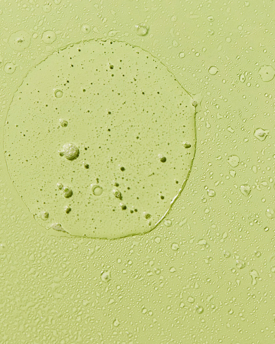 Close-up texture swatch of green aloe vera hair oil mist with fine droplets.