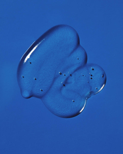 Clear dollop of Pequi styling gel swatched on a bright blue background, showing its glossy, bubble-flecked texture.
