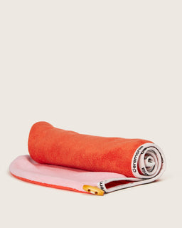 Ceremonia microfiber hair towel in coral and pink, rolled with branded trim and wooden button.