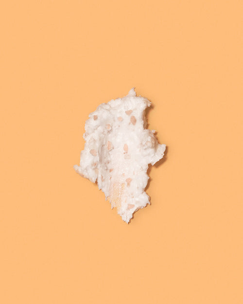 Swatch of whipped white papaya scalp scrub with pink salt exfoliating granules on an orange background.