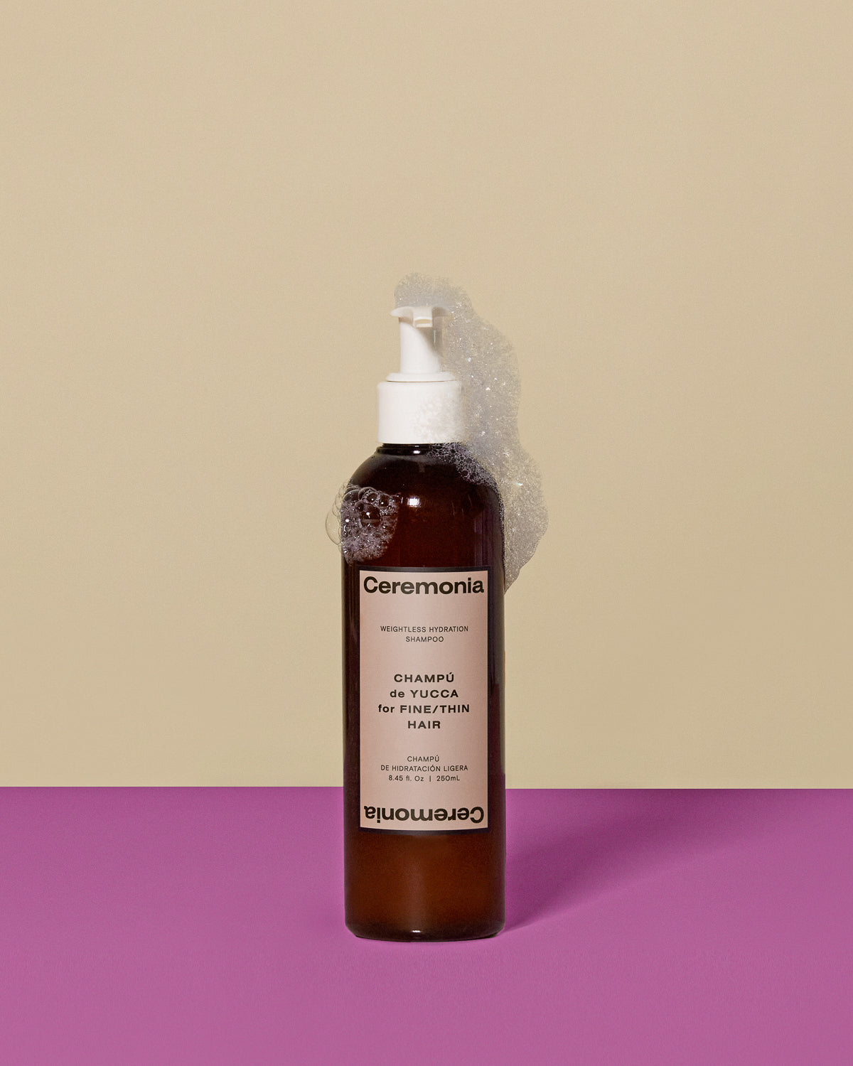 Ceremonia Weightless Hydration shampoo pump bottle with sudsy bubbles on beige and magenta backdrop.